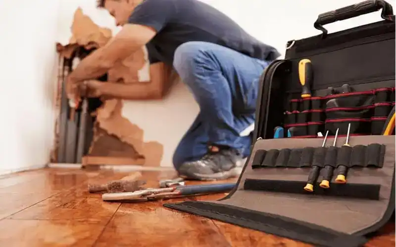 plumber digging into a wall to fix a pipe leak